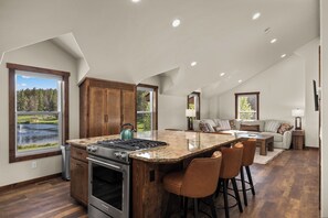A kitchen with a large island, wooden cabinets, and a view of a lake. - Strawberry Moon in Whitefish with Hot Tub (Whitefish)