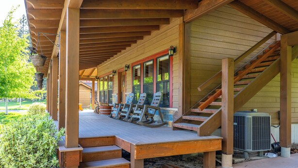 A covered outdoor area with a wooden deck, steps leading to a porch, and outdoor seating. - Strawberry Moon in Whitefish with Hot Tub (Whitefish)