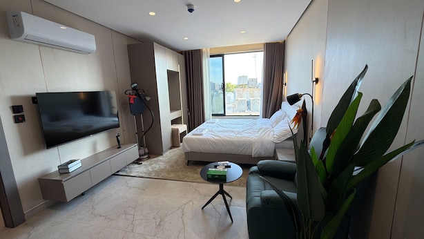 Une chambre d’hôtel moderne équipée d’un téléviseur à écran plat, d’un lit, d’un canapé, d’une table basse et d’une grande plante.