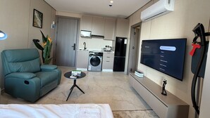 Un salon moderne avec un canapé, une table basse, un téléviseur et une cuisine en arrière-plan.