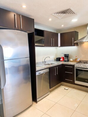 A modern kitchen with stainless steel appliances, dark wooden cabinets, a granite countertop, and a built-in microwave. - Venetian 1BR Panoramic Oceanview (Puerto Vallarta)