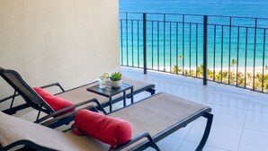 Een balkon met twee loungestoelen, een tafeltje met een plant en uitzicht op de oceaan.