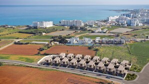 Eine Luftaufnahme eines Küstenwohngebiets mit moderner Bebauung, einem Jachthafen und freiem Blick auf das Meer.