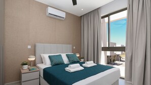 Ein modernes Hotelzimmer mit einem großen Bett, einem Nachttisch mit Lampe, einem Blumentopf und Blick ins Freie.