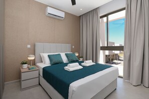 Ein modernes Hotelzimmer mit einem großen Bett, einem Nachttisch mit Lampe, einem Blumentopf und Blick ins Freie.