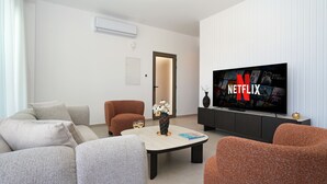 Ein modernes Wohnzimmer mit Sofa, Sessel, Couchtisch und einem Fernseher mit Netflix-Logo.