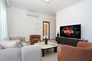 Ein modernes Wohnzimmer mit Sofa, Sessel, Couchtisch und einem Fernseher mit Netflix-Logo.