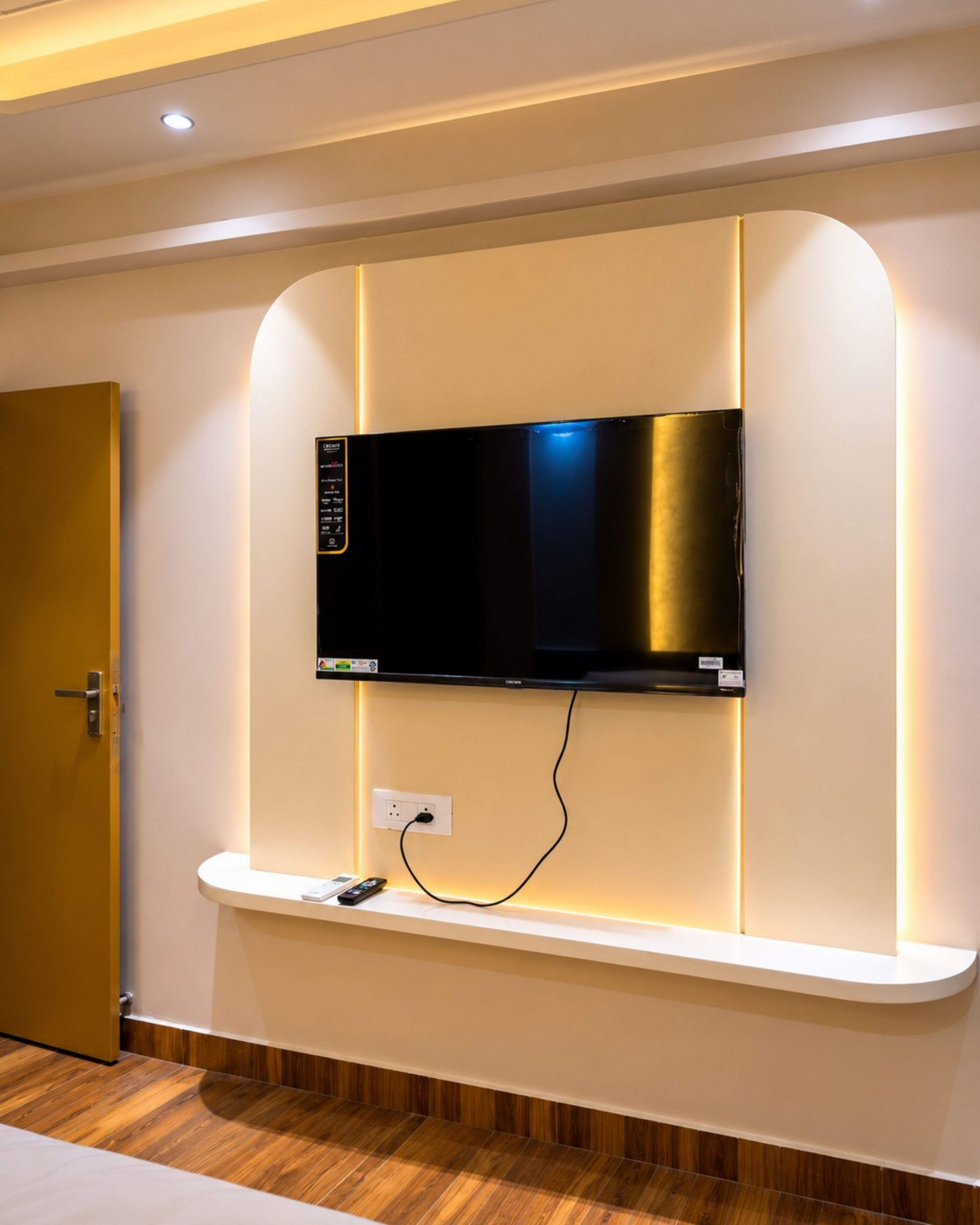 A modern room with a mounted flat-screen TV, a built-in shelf, and a wooden floor.