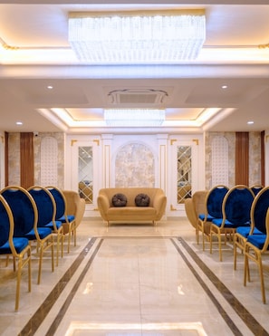A hotel lobby with a central sofa, blue chairs, a chandelier, and a patterned wall. - The Masara Manar (Gwalior)
