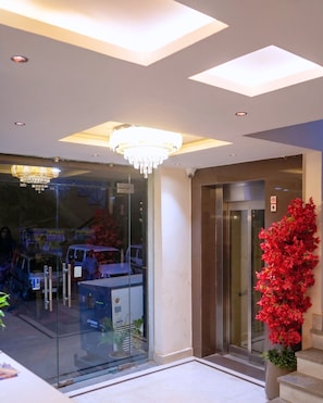 A modern lobby with a glass entrance, a chandelier, an elevator, and a red flower arrangement. - The Masara Manar (Gwalior)