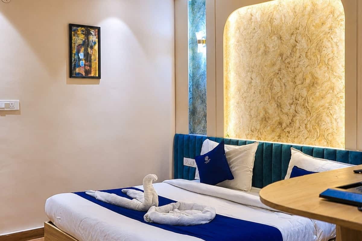 Habitación de hotel con suelo de madera, cama con ropa de cama azul y blanca, mesa redonda de madera y un ventanal con vistas.