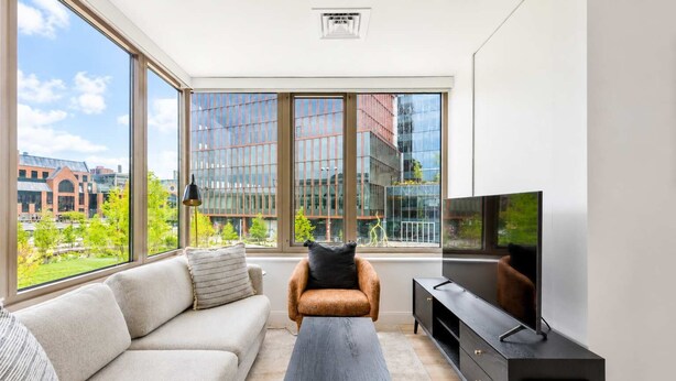 En moderne stue med sofa, sofabord, fjernsyn og store vinduer med udsigt over byen.