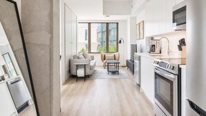 Et moderne køkken med rustfrie stålapparater, et spiseområde med sofa og bord, samt store vinduer med udsigt ud