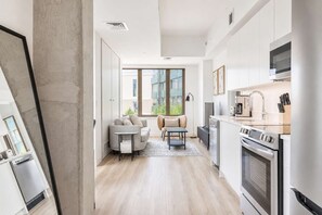 Eine moderne Küche mit Edelstahlgeräten, ein Essbereich mit Sofa und Tisch sowie große Fenster mit Blick ins Freie.