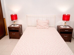 Ein Schlafzimmer mit einem weißen Bett, zwei Nachttischen mit Lampen, einem Holzschrank und einer gemusterten Tagesdecke.
