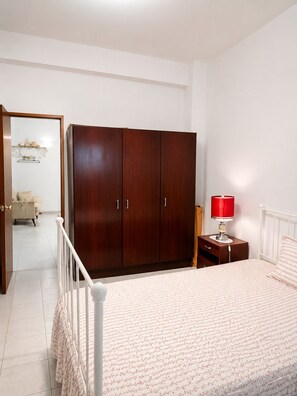 A bedroom with a bed, a wardrobe, a nightstand with a lamp, and a bathroom visible in the background. - 2-bedroom Appartment in Center of SB Messines 

Between Mountains and Beaches (São Bartolomeu de Messines)