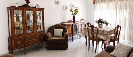 Una sala de estar con un sofá marrón, un mueble de madera con puertas de vidrio, una mesa de comedor con sillas y una araña.