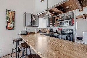 Una cocina con encimera de madera, taburetes de bar, microondas, horno y una lámpara colgante.