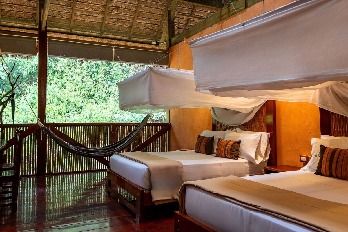 A room with two beds, a hammock, and a thatched roof.