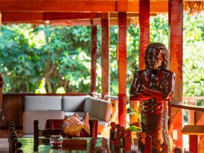 Una estatua, un pez y una mesa con diversos objetos en una habitación que da a zonas verdes.