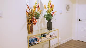 A hallway with a round mirror, a vase with flowers, a glass shelf with books, and a door.