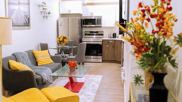 Een moderne woonkamer met een bank, poefs, een glazen salontafel en een eethoek met stoelen.