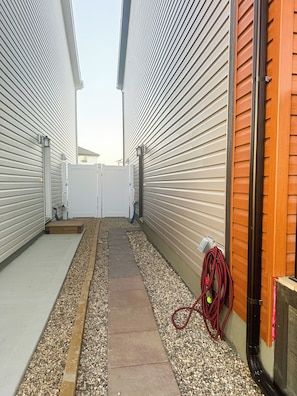 A narrow pathway flanked by buildings with siding and a wooden door, leading to a gated entrance. - Private Guest Suite in Regina, SK | Quiet, Clean & Comfortable (Regina)