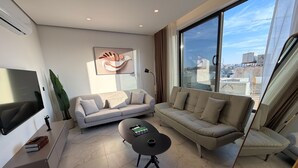 Una sala de estar moderna con sofá, mesa de centro, televisor y un amplio ventanal con vista a la ciudad.