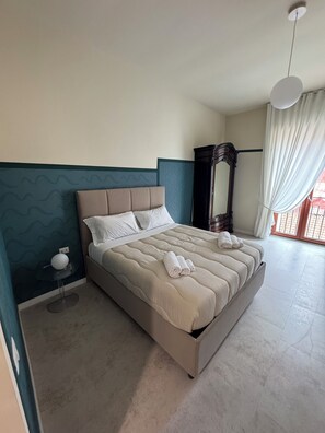 A bedroom with a bed, a bedside table with a lamp, a wardrobe, and a view of the outdoors. - Napolispacca Holiday Home by H4H (Napoli)