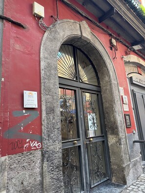 A building facade with a red wall, a stone archway, and a black door with decorative ironwork. - Napolispacca Holiday Home by H4H (Napoli)