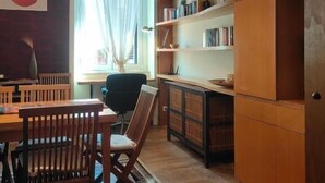 Een kamer met een houten eettafel, stoelen, een boekenkast en een groot raam met gordijnen.