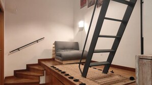 Een trap met een houten afwerking, een grijze bank en een zwarte ladder die tegen de muur staat.