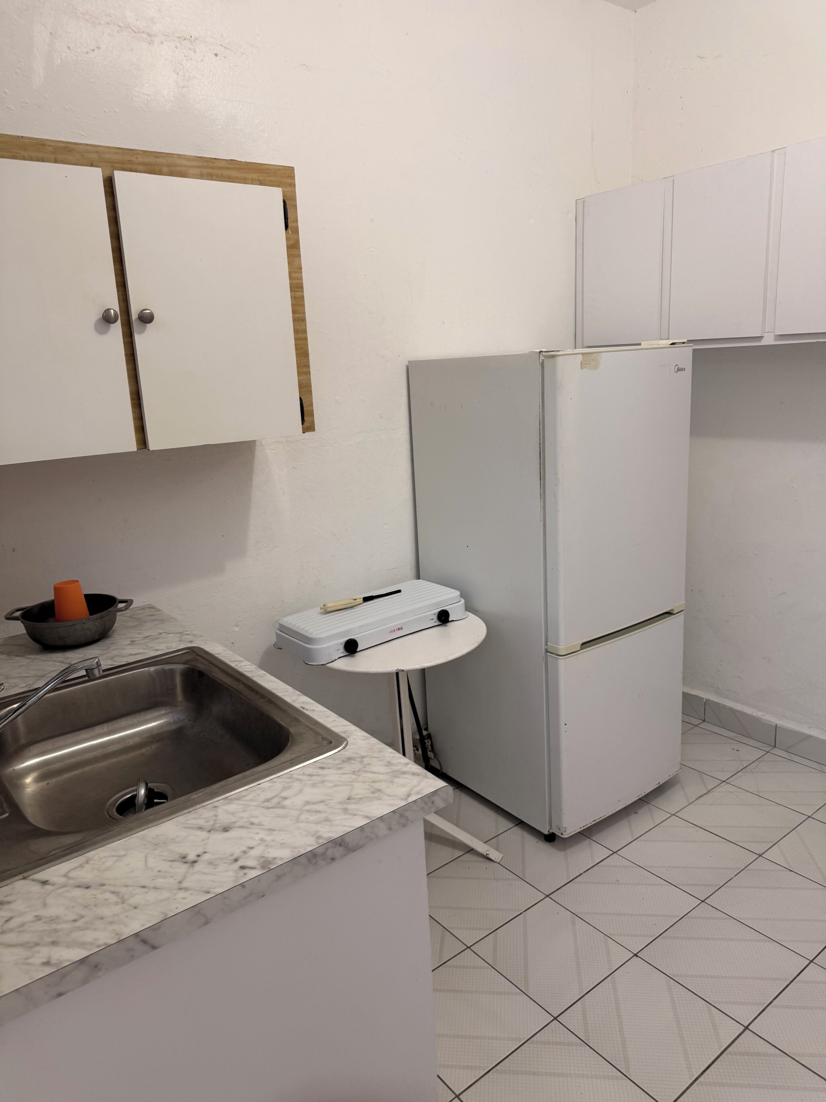 A kitchen with a sink, a white refrigerator, and a small table with a kettle.