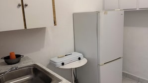 Cozinha com pia, geladeira branca e uma mesa pequena com chaleira.