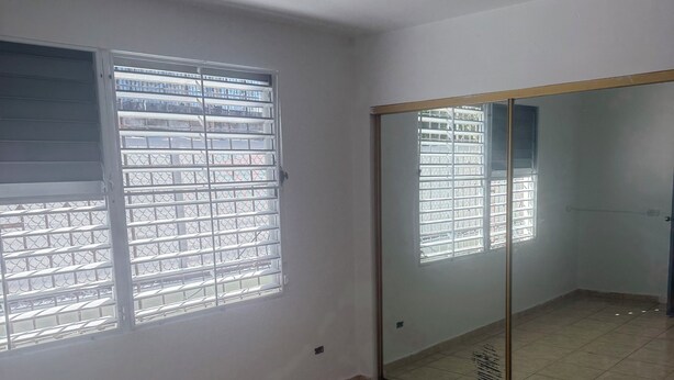 Quarto com piso de azulejos, porta de vidro deslizante e janelas com grades.