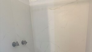 Pequena área de chuveiro fechada, com azulejos de mármore branco e chão com padrão hexagonal.