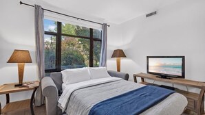 Une chambre à coucher avec un lit, deux tables de chevet, une télévision et une fenêtre avec des rideaux.