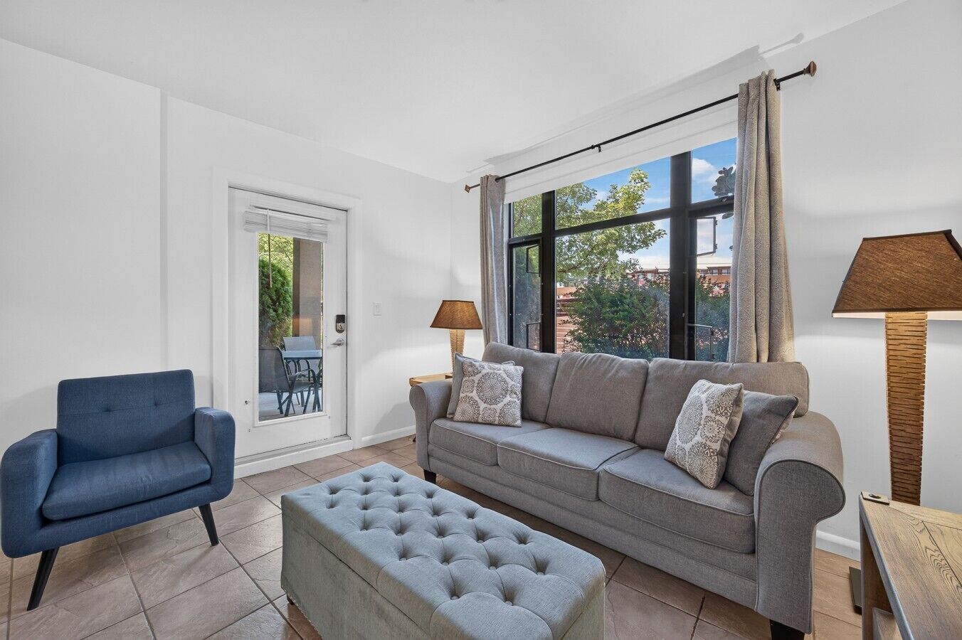 Una sala de estar con sofá, reposapiés, sillón y ventana con cortinas.
