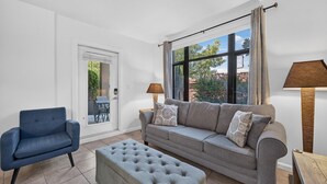 Un salon comprenant un canapé, un pouf, un fauteuil et une fenêtre avec des rideaux.