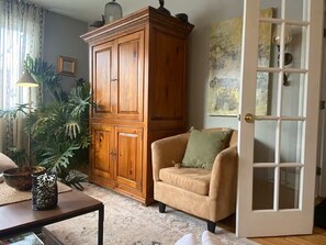 A living room with a wooden cabinet, a beige sofa, a glass door, and a plant. - Warm little jewels! (Longueuil)