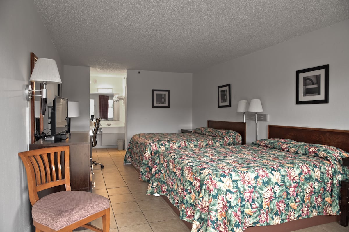 A hotel room with a bed, two bedside tables, a chair, a desk with a lamp, and a mirror.