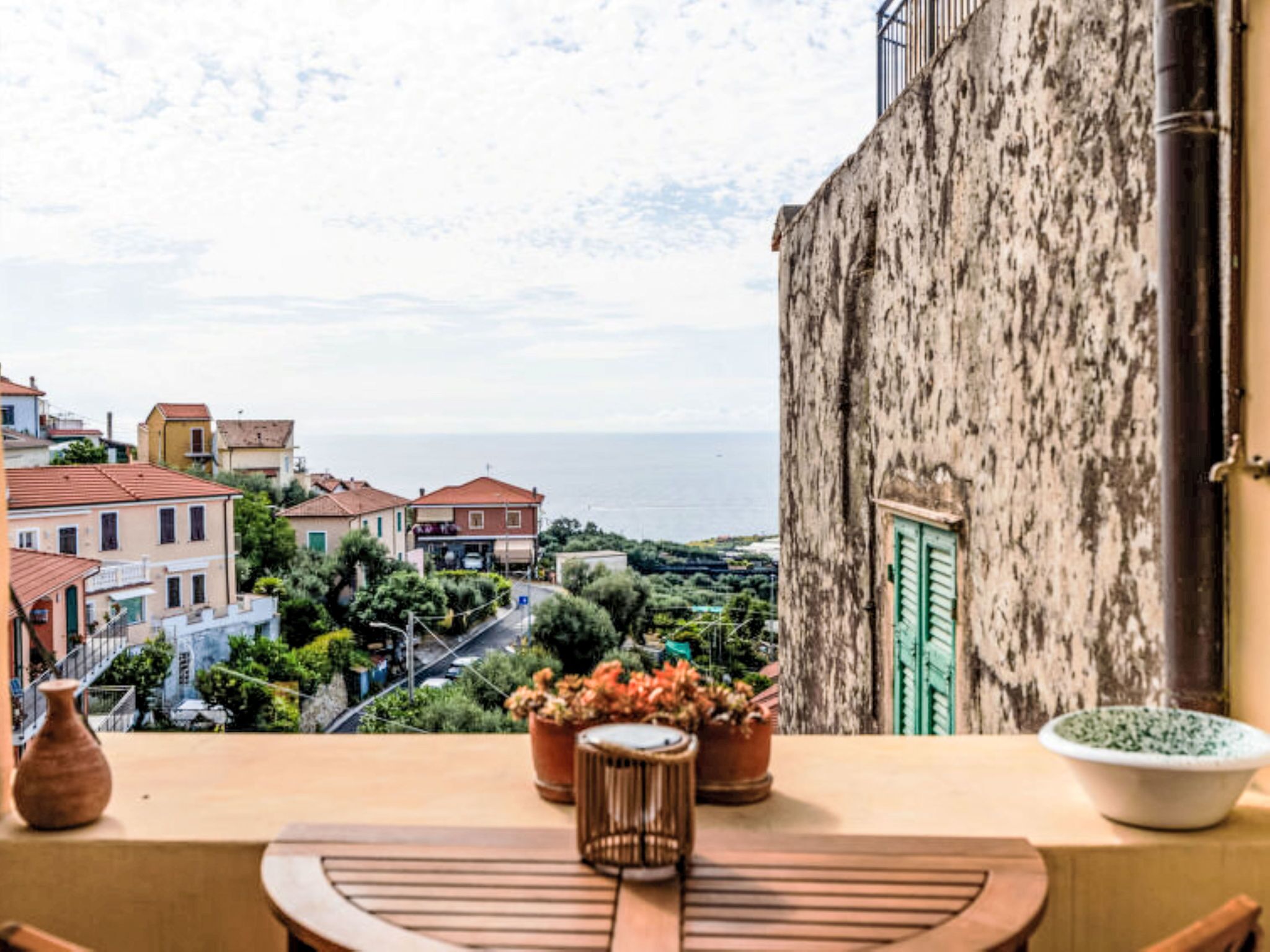 Un balcon donnant sur une ville côtière, un bâtiment à l’aspect rustique et des plantes en pot.