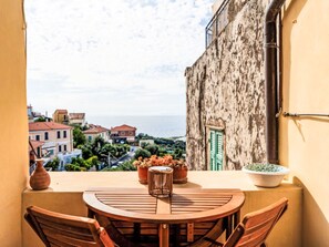 Ein Balkon mit Holztisch und -stühlen, Topfpflanzen und Blick auf eine Küstenstadt.