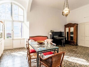 Ein Essbereich mit einem Glastisch, Korbstühlen, einem Klavier und einem großen Fenster.