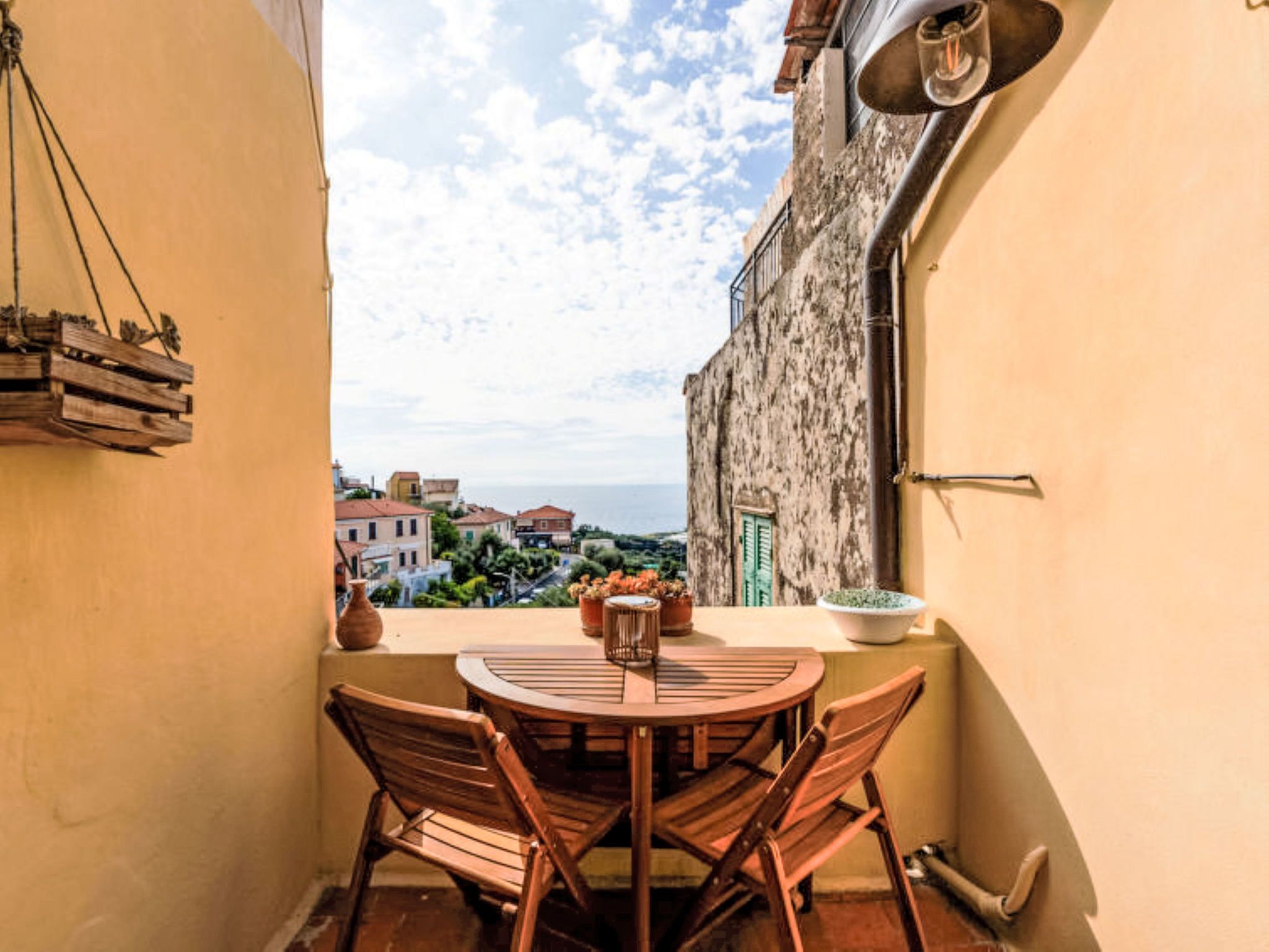 Un balcon avec une table et des chaises, un luminaire suspendu et une vue sur la mer et les bâtiments.