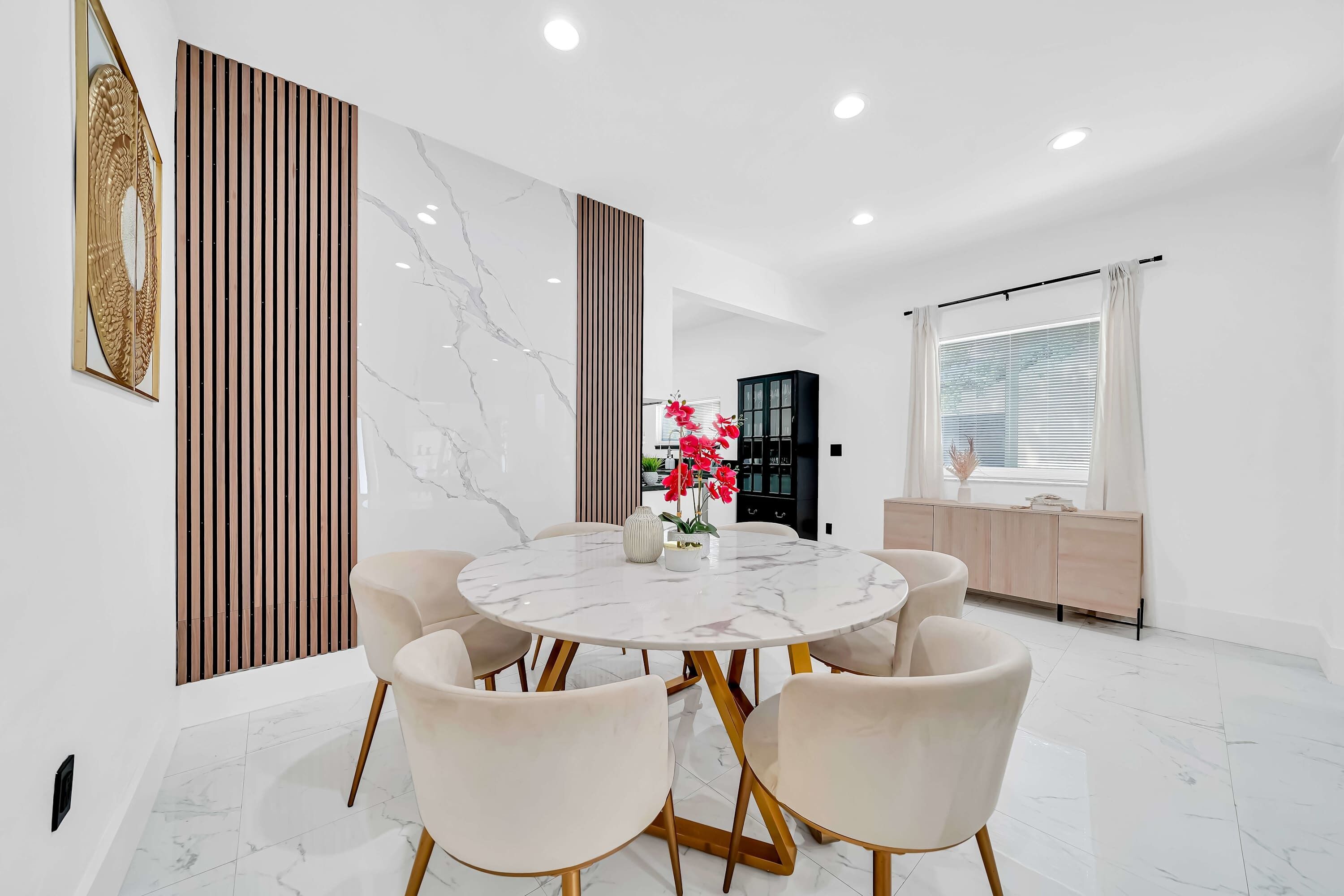 A modern dining room with a marble table, six chairs, and a decorative vase with flowers.