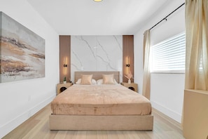 Ein modernes Schlafzimmer mit einem großen Bett, einem Marmorkopfschild und einem Bild an der Wand.