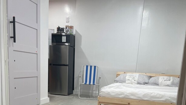A compact room with a bed, a chair, a kitchenette, and a door. - Private room in tiny home in Brooklyn, New York (Brooklyn)