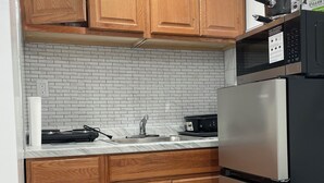 A kitchen with wooden cabinets, a stainless steel refrigerator, a microwave, and a tiled backsplash. - Private room in tiny home in Brooklyn, New York (Brooklyn)