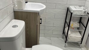 A bathroom with a toilet, sink, and a shelf with towels. - Private room in tiny home in Brooklyn, New York (Brooklyn)